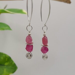 May include: A pair of silver earrings with pink gemstone accents. The earrings feature a spiral design and three pink gemstones on each earring.