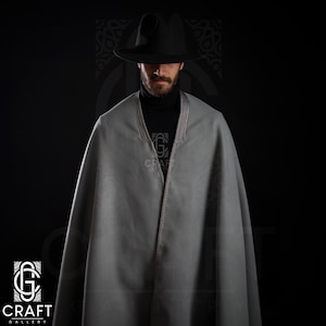 May include: A gray wool cape with a black hat and a black turtleneck. The cape has a silver trim around the neckline and a silver button closure.