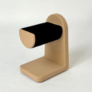 May include: A tan-coloured jewellery stand with a black velvet ring holder. The stand has a rounded base and a curved arm.