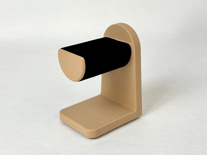 May include: A tan-coloured jewellery stand with a black velvet ring holder. The stand has a rounded base and a curved arm.