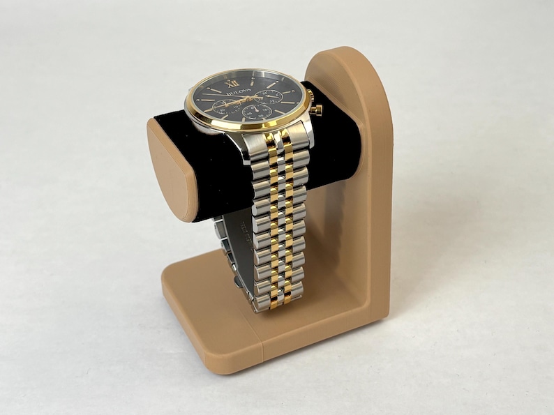 May include: A gold and silver watch with a black face and a brown watch stand.