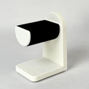 May include: White watch stand with a black velvet cushion for holding a watch.