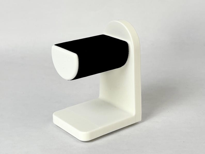 May include: White watch stand with a black velvet cushion for holding a watch.