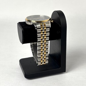 May include: A black watch stand with a gold and silver watch on it.