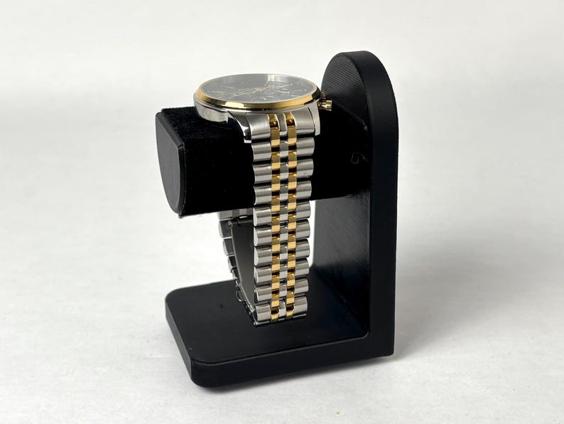 May include: A black watch stand with a gold and silver watch on it.
