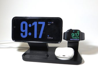 May include: A black charging stand with a white wireless charging pad for earbuds, a black phone stand with a black phone displaying the time 9:17, and a black Apple Watch displaying the time 9:17.