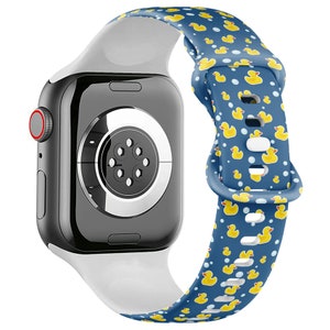 May include: A white and blue Apple Watch band with a pattern of yellow rubber ducks. The band is made of silicone and has a buckle closure.