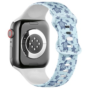 Può includere: Un cinturino per Apple Watch bianco con sfondo azzurro chiaro e un motivo ripetitivo di tartarughe marine blu. Il cinturino è in silicone e ha una finitura liscia.
