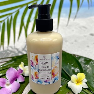 May include: A beige bottle of Cascia Body Revive Leave In Conditioner with a black pump top. The label features floral watercolor art and the text "REVIVE Leave In Conditioner". The bottle is 8 oz.