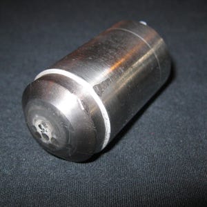 May include: A cylindrical metal object with a brushed finish and a rounded end featuring a series of small, circular perforations. A thin white ring separates the main body from the domed, perforated cap, creating a distinct two-part structure.