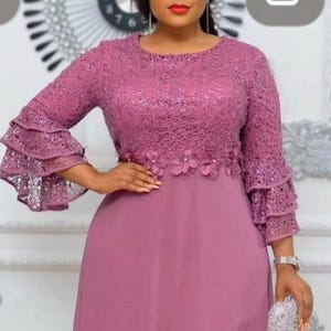 May include: A mauve formal dress with a lace bodice and long sleeves with ruffled cuffs. The dress has a flowing skirt and is accessorized with a silver clutch and watch. Suitable for special occasions.