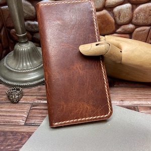 May include: A brown leather wallet with white stitching. The wallet is rectangular and appears to be closed. The leather has a distressed look. The wallet is on a gray surface.