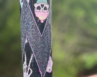 May include: A black and purple glitter tumbler with a skull cupcake, a peace sign skeleton hand, and a purple alien design.