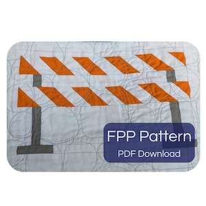Pode incluir: Um bloco de colcha de tecido branco com uma construção de peças de uma barreira de construção com listras diagonais laranja e brancas e suportes cinzas. O fundo tem costuras circulares. O texto diz FPP Pattern PDF Download.