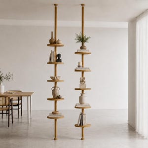 May include: Two floor-to-ceiling tension pole shelving units made of light-toned wood. Each unit features six circular shelves arranged vertically, holding various decorative items including ceramic vases, books, a small bust, and a green plant.