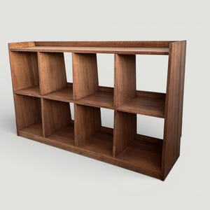 May include: A wooden storage shelf with eight cubby holes. The shelf is made of dark brown wood and has a rectangular shape. The top of the shelf has a flat surface, and the cubby holes are evenly spaced.