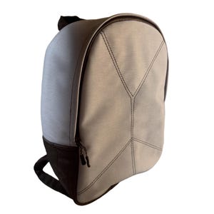 以下が含まれることがあります： 黒いアクセントが付いた、明るい灰色のバックパック。 バックパックは、湾曲した上部、黒いジッパー、黒いハンドルが特徴です。 バックパックの前面には、ステッチされた幾何学模様があります。 バックパックの底と背面は黒です。