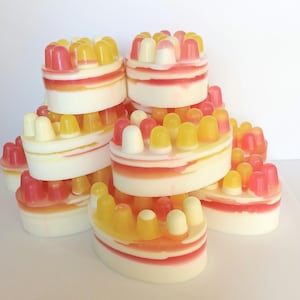 May include: A stack of colourful, heart-shaped soaps with a bumpy texture. The soaps are layered in a pyramid shape, with the top soap being pink and white, and the bottom soap being yellow and white.