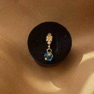 May include: A gold nose ring with a small blue crystal dangling from it. The nose ring is decorated with small clear rhinestones.