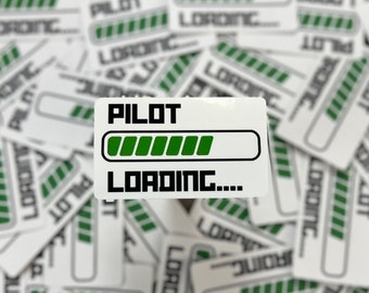 May include: A white sticker with black text that reads "PILOT LOADING..." with a green progress bar underneath. The sticker is surrounded by other stickers with similar designs.