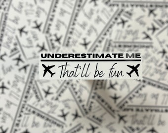 May include: Black and white sticker with the text "UNDERESTIMATE ME That'll be fun" and a small airplane graphic on each side.