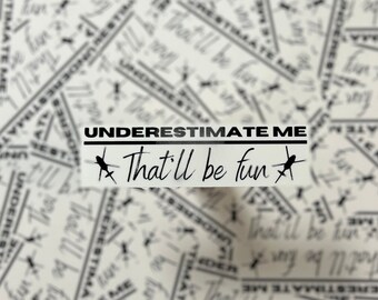 May include: A white sticker with the text "UNDERESTIMATE ME" above "That'll be fun" in a handwritten font. The sticker has a black border and is set against a background of similar text.
