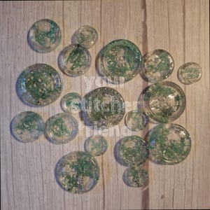May include: Assortment of clear resin buttons with green and silver glitter embedded inside. The buttons are various sizes and shapes.