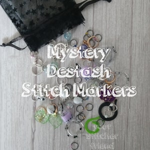 May include: A black mesh bag filled with a variety of colorful stitch markers. The bag is labeled "Mystery Destash Stitch Markers" and "your stitcher friend".