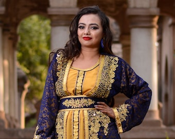 May include: A long, blue and gold kaftan with intricate embroidery. The kaftan has a high neckline and long sleeves. The fabric is sheer and has a floral pattern. The kaftan is belted at the waist with a gold belt.