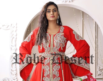 May include: A red kaftan with silver and gold embroidery. The kaftan has a long, flowing skirt and long sleeves. The fabric is sheer and the embroidery is intricate. The kaftan is worn by a woman with long, dark hair.