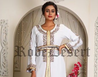 May include: A white maxi dress with gold and maroon embroidery. The dress has a long, flowing skirt and a fitted bodice. The dress is accented with a gold belt and a gold and maroon trim.
