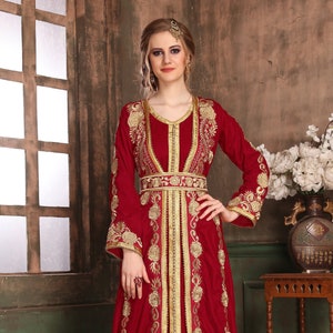 K&ouml;nnte beinhalten: Eine lange, rote Kaftan mit goldener Stickerei mit floralen Mustern. Die Kaftan hat einen V-Ausschnitt und lange &Auml;rmel. Sie ist in der Taille geg&uuml;rtet und hat einen Schlitz vorne.