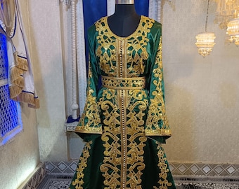 May include: A long, emerald green dress with gold embroidery and a matching gold belt. The dress features intricate floral patterns and bell sleeves. The garment is displayed on a mannequin.