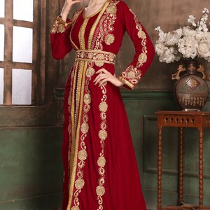 K&ouml;nnte beinhalten: Ein langes, rotes Samtkleid mit goldener Stickerei. Das Kleid hat einen langen Schlepp und ein tailliertes Oberteil. Die Stickerei zeigt florale Muster und komplizierte Muster.