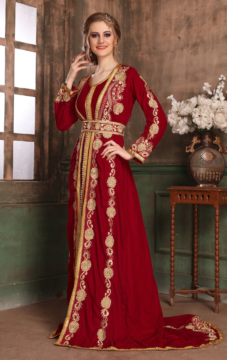 K&ouml;nnte beinhalten: Ein langes, rotes Samtkleid mit goldener Stickerei. Das Kleid hat einen langen Schlepp und ein tailliertes Oberteil. Die Stickerei zeigt florale Muster und komplizierte Muster.