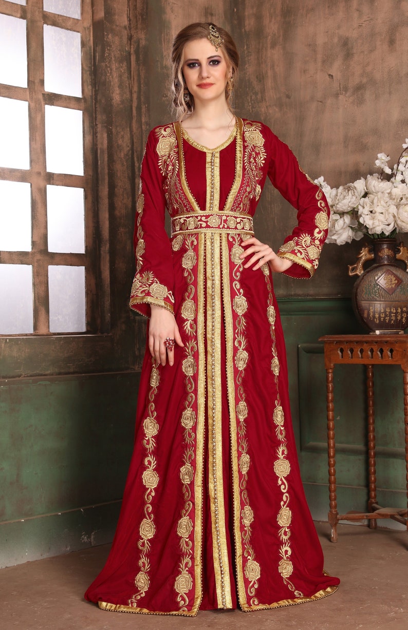 K&ouml;nnte beinhalten: Eine lange, rote Kaftan mit goldener Stickerei mit floralen Mustern. Die Kaftan hat einen V-Ausschnitt und lange &Auml;rmel. Sie ist in der Taille geg&uuml;rtet und hat einen Schlitz vorne.