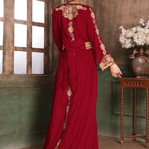 K&ouml;nnte beinhalten: Ein langes, burgunderfarbenes Samtkleid mit goldener Stickerei. Das Kleid hat einen langen Schlepp und einen G&uuml;rtel in der Taille.