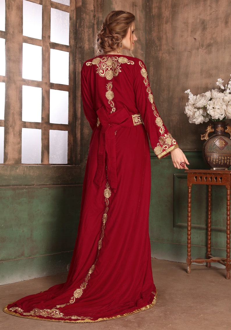 K&ouml;nnte beinhalten: Ein langes, burgunderfarbenes Samtkleid mit goldener Stickerei. Das Kleid hat einen langen Schlepp und einen G&uuml;rtel in der Taille.