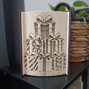 May include: A folded book art sculpture featuring a stack of five gift boxes with bows. The pages are precisely folded to create the three-dimensional shape of presents, with visible patterns of stripes, dots, and stars on the gift box surfaces.