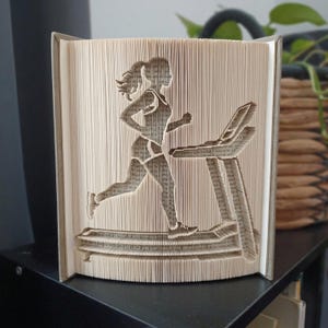 Op de afbeelding: Een gevouwen boekkunstsculptuur met het silhouet van een persoon die op een loopband rent. Het ontwerp is gemaakt door de individuele pagina's van een hardcover boek nauwkeurig te vouwen om de vorm van de hardloper en machine te onthullen.