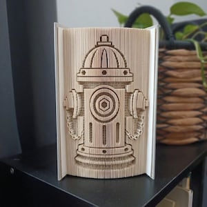 Puede incluir: Una escultura de libro con un diseño de boca de incendio creado doblando las páginas de un libro. Los bordes de papel beige están manipulados con precisión para formar la silueta de una boca de incendio con una válvula central y salidas.