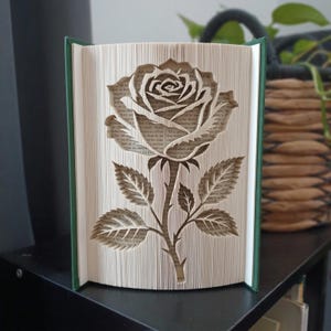 Peut inclure: Une sculpture de livre représentant une rose créée en pliant les pages d'un livre. La rose, y compris sa tige et ses feuilles, est formée par la disposition précise des bords du papier, révélant le texte imprimé sur les pages intérieures.