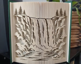 May include: A book sculpture featuring intricate folded pages that form a three-dimensional waterfall scene. The design includes layered rock formations, a cascading water effect, and evergreen trees on both sides, all crafted from the pages of a book.