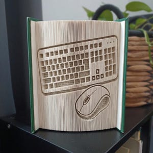 Könnte beinhalten: Eine Buchskulptur mit gefalteten Seiten, die die Form einer Computertastatur und einer Computermaus bilden. Das Buch hat einen dunkelgrünen Einband und die Seiten sind cremefarben, was die komplexe Papierfalttechnik zur Gestaltung verdeutlicht.