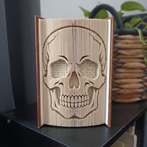 Op de afbeelding: Een boeksculptuur met een menselijk schedelontwerp, gemaakt door de individuele pagina's van een hardcover boek nauwkeurig te vouwen. De beige papieren randen zijn gevormd om de oogkassen, neusholte en tanden van de schedel te vormen.