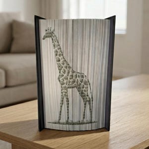 Könnte beinhalten: Dekorative Buchskulptur mit einem Giraffen-Design. Die Giraffenillustration ist in Graustufen gehalten und wird durch die Seiten des Buches gebildet. Das Buch hat einen schwarzen Rahmen und steht auf einer Holzoberfläche.