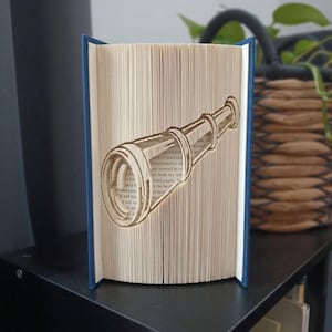 Könnte beinhalten: Eine Buchskulptur mit gefalteten Seiten, die die Form eines Fernrohrs bilden. Das Buch hat einen dunkelblauen Einband und die cremefarbenen Innenseiten zeigen gedruckten Text, der durch die präzise Falttechnik des Papiers sichtbar wird.