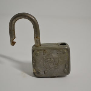 May include: A silver padlock with a square body and a curved shackle. The padlock has a decorative design with a winged creature and the text "1776" on the front.