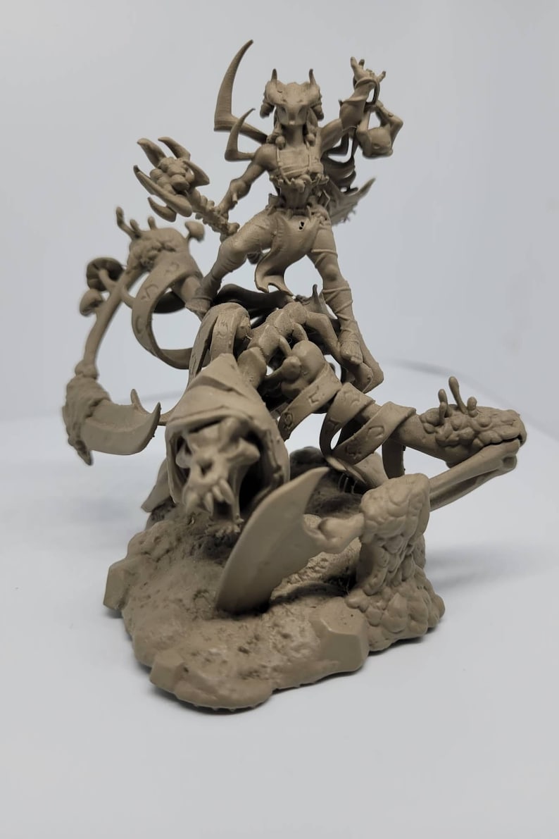 May include: A brown, 3D printed miniature of a female figure with horns and wings standing on a skeletal creature with a scythe. The figure is holding a staff with a skull at the top. The miniature is set on a base of textured brown plastic.