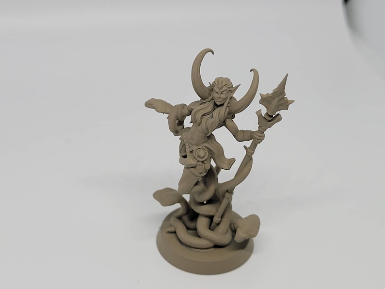May include: A brown painted miniature figurine of a female figure with horns and a staff, standing on a base with snakes wrapped around it.
